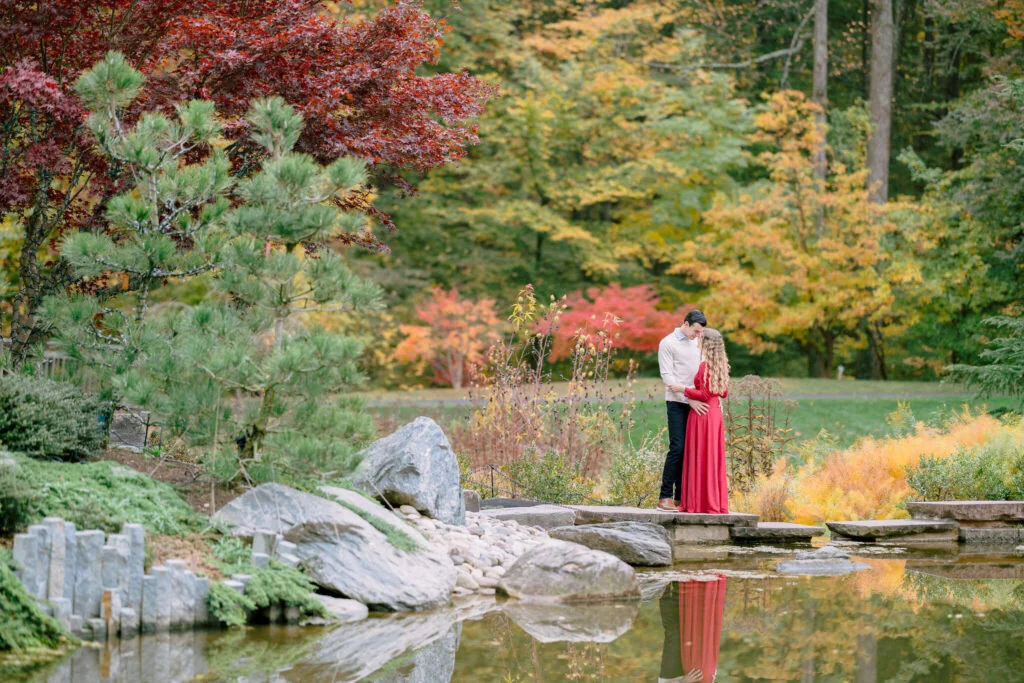 Couple surrounded by colorful fall foliage beside a reflective pond