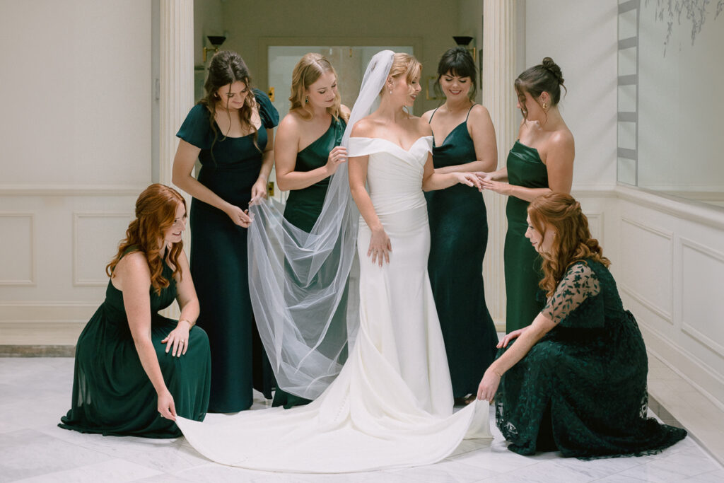 The picture showcases bridesmaids in green attire with her bride in the center wearing a wedding gown and white veil, adding a touch of grace to the wedding ceremony.