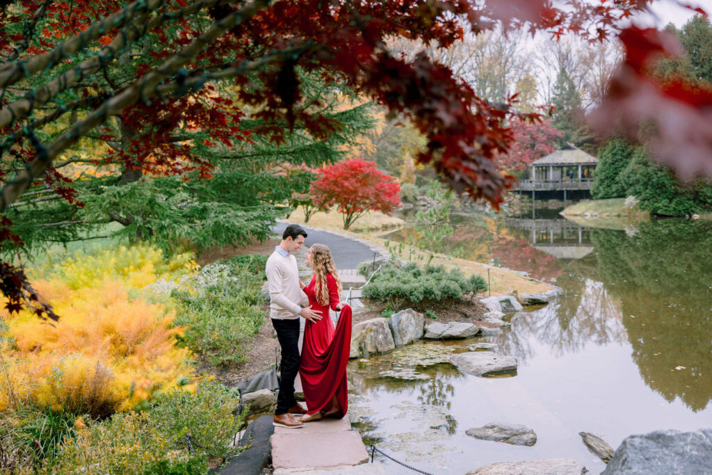 A couple smiles for their engagement photos in the Brookside gardens, surrounded by the vibrant colors of fall foliage.