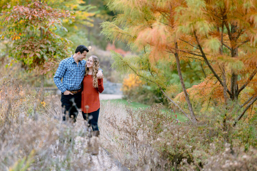 A couple walking in a candid picture for their engagement photos amidst lush greenery and colorful flowers at the Brookside gardens of Maryland.