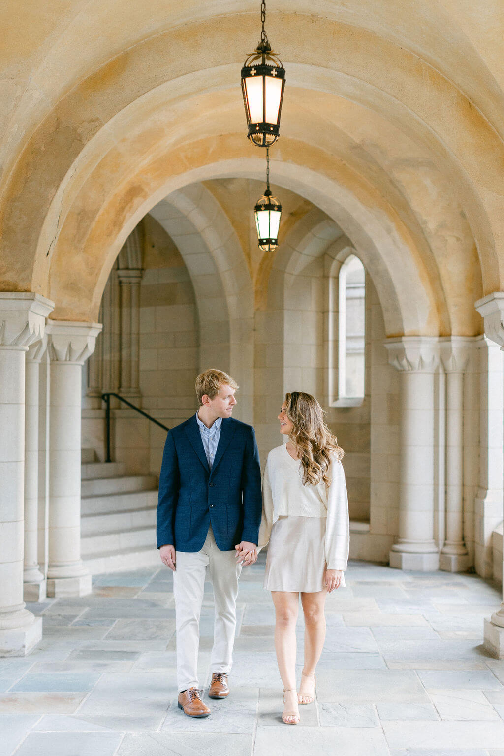 Engagement Session at Washington's National Cathedral: Joan and Richard share a moment, walking hand-in-hand under the archways, with the warm glow of a lantern above them, captured by Get Ready Photo.