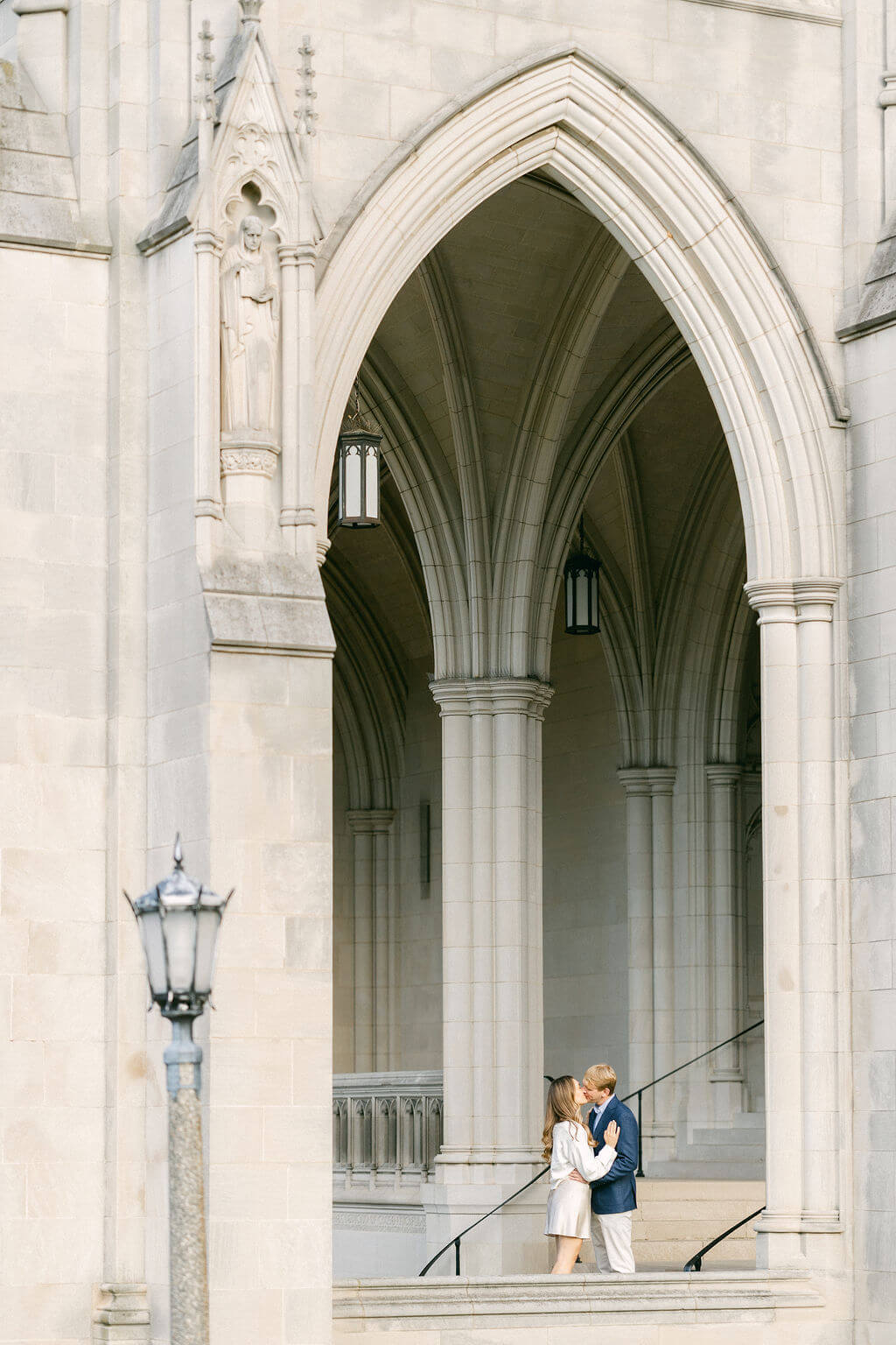 A photo of a couple sharing a moment on the steps within an arched corridor of the Washington National Cathedral, with the intricate gothic architecture surrounding them, taken by Get Ready Photo